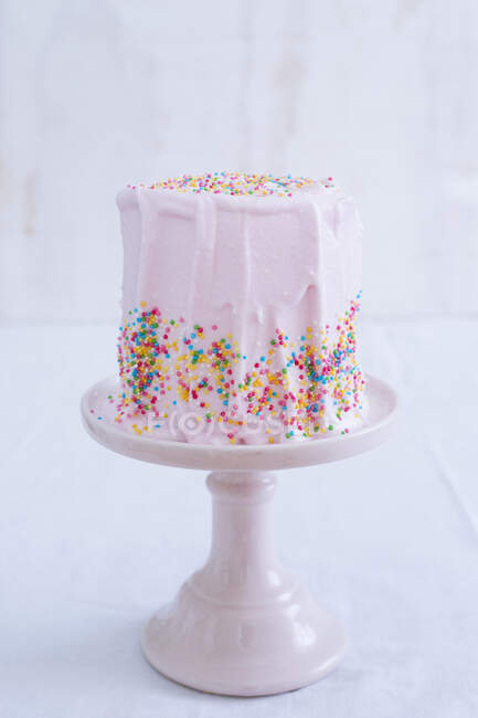 Un gâteau rose givré avec des paillettes colorées sur un stand rose — Photo de stock