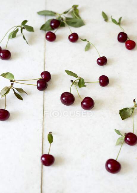 Fresh cherries with green leaves on white stone surface — Stock Photo
