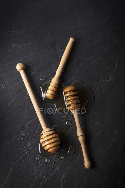 Three honey dippers with honey on a black slate — Stock Photo