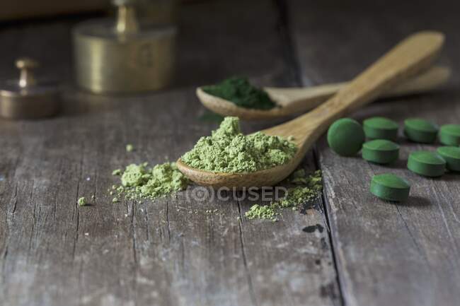 Spirulina tablets and spirulina powder on wooden spoons — Stock Photo