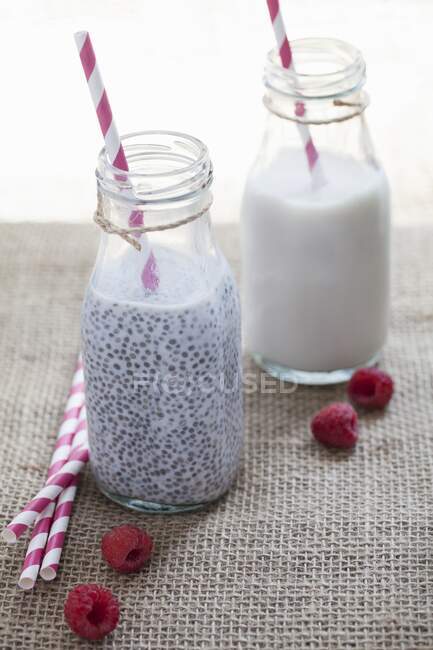 Семена чиа с миндальным молоком в бутылках и малиной на столе — стоковое фото