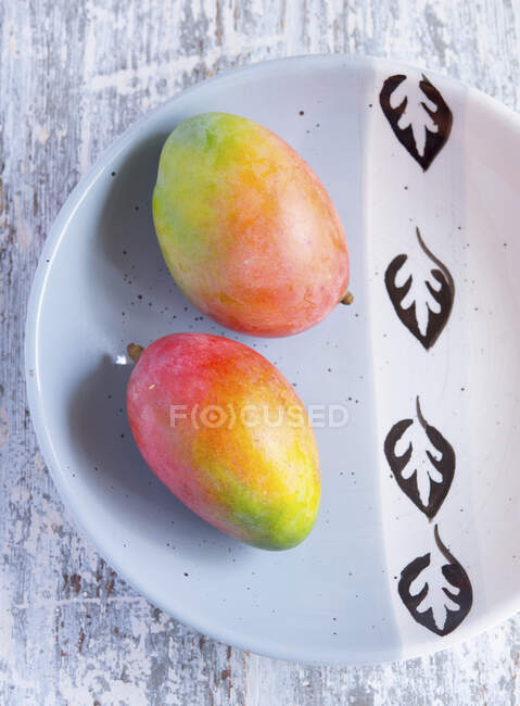 Deux mangues entières sur plaque céramique avec motif de feuilles — Photo de stock
