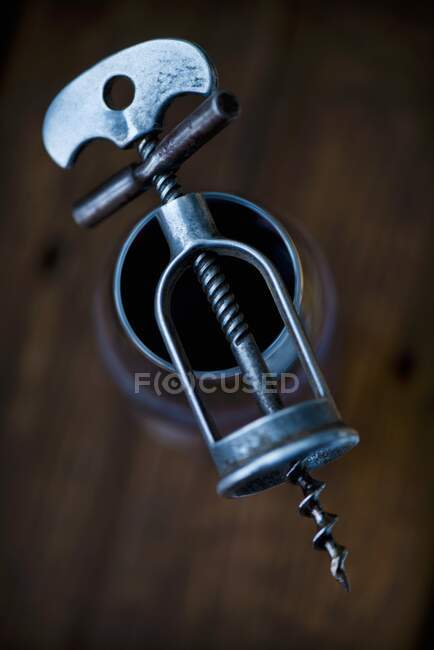 An antique corkscrew on top of a glass of red wine — Stock Photo