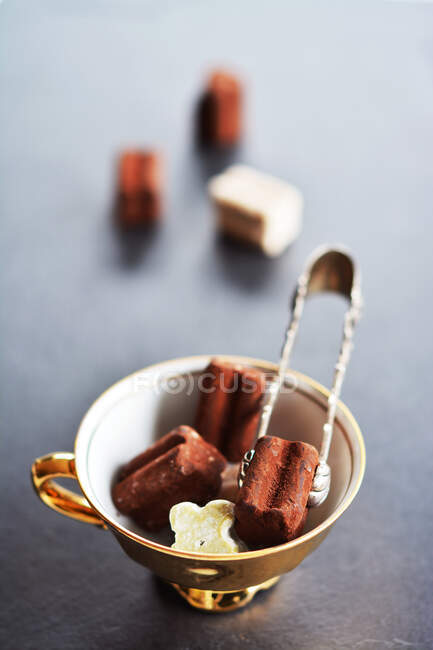 Pralines pequenos em uma xícara dourada com pinças praline — Fotografia de Stock