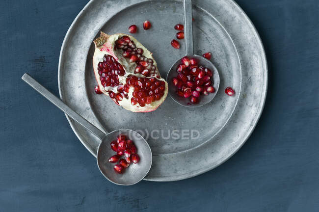 Pomegranate pieces and seeds on a pewter plate with two metal spoons (top view) — Stock Photo