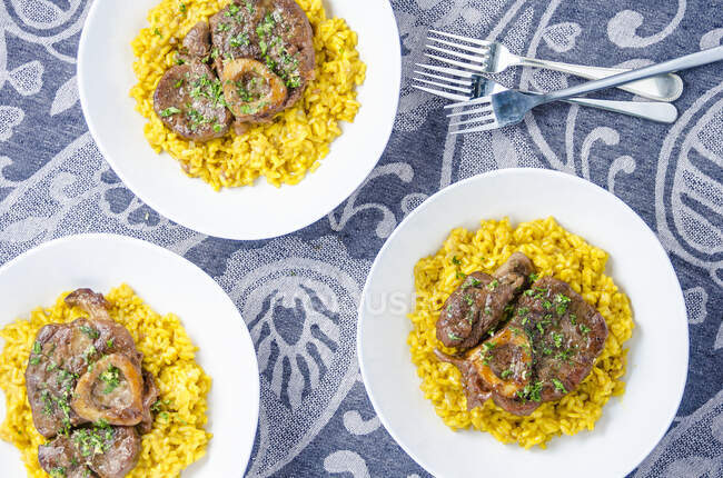 Three portions of osso buco milanese meat on a yellow saffron risotto garnished with fresh chopped parsley — Stock Photo
