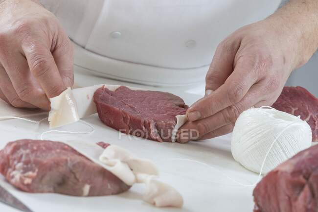 Um chef embrulhando um filé de bife em bacon — Fotografia de Stock