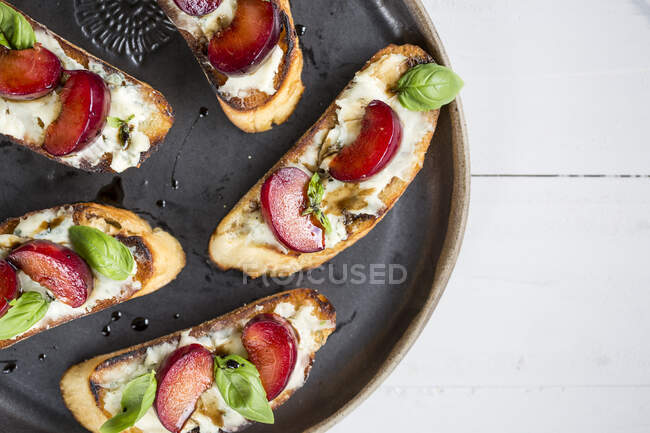 Crostini con prugne e foglie di basilico sul piatto — Foto stock