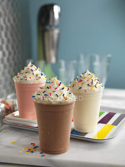 Três batidos de leite diferentes com creme e polvilhas de açúcar coloridas — Fotografia de Stock