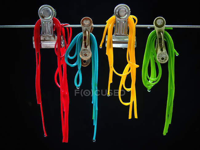 Different colored spaghetti hung from clips in front of a black background — Photo de stock