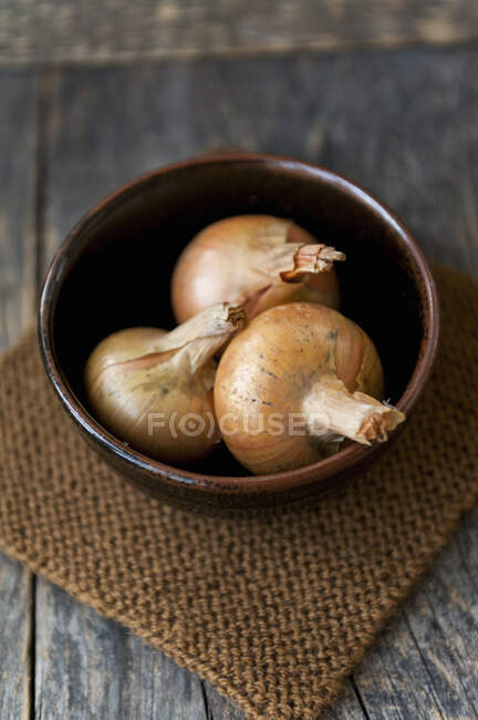 Três cebolas em uma tigela marrom — Fotografia de Stock
