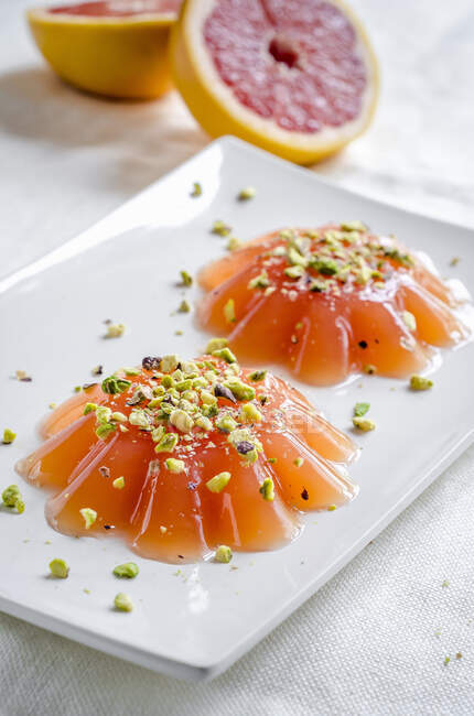 Розовые грейпфрутовые желе с фисташковыми орехами подаются на тарелке — стоковое фото