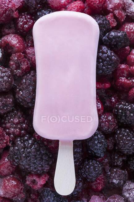 Ice lolly on frozen raspberries and blackberries — Stock Photo