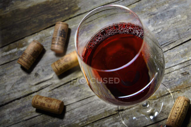 A red wine glass and corks on a rustic wooden table — Stock Photo