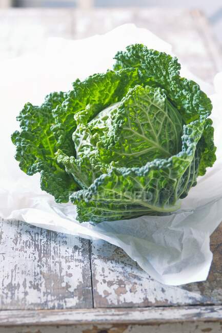 A savoy cabbage on paper and a wooden background — Stock Photo