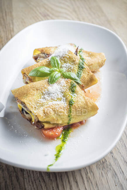 Egg crepes roll with vegetables and mushrooms in a tomato sauce with pesto dressing and a sprinkle of parmesan chees — Stock Photo