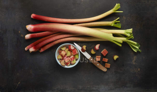 Rhubarb stems and chopped rhubarb in a bowl with a knife — Stock Photo