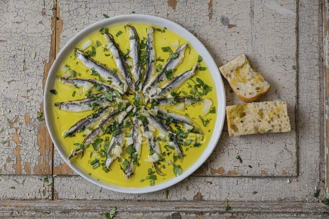 Anchovies in garlic oil served with herbs and bread (top view) — Stock Photo