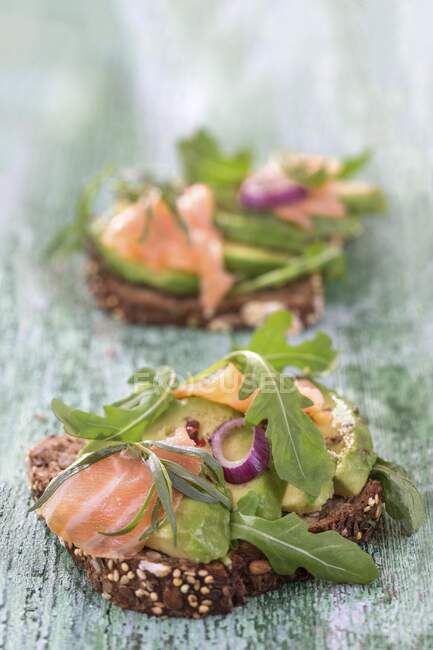 Wholegrain bread topped with avocado slices, salmon and rocket — Stock Photo