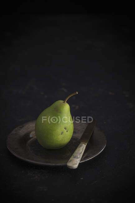 Green pear on metal plate with knife — Stock Photo