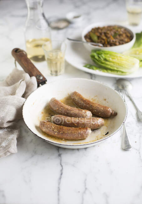 Sausages in ceramic frying pan on table — Stock Photo