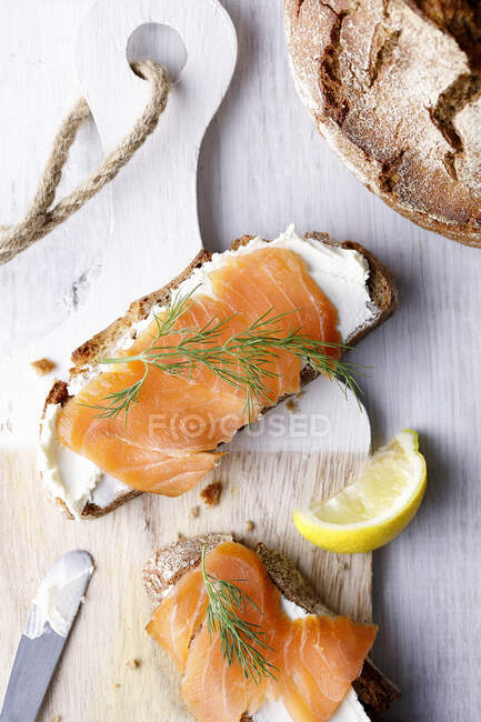 Two slices of bread with cream cheese, salmon and dill on wooden board — Stock Photo