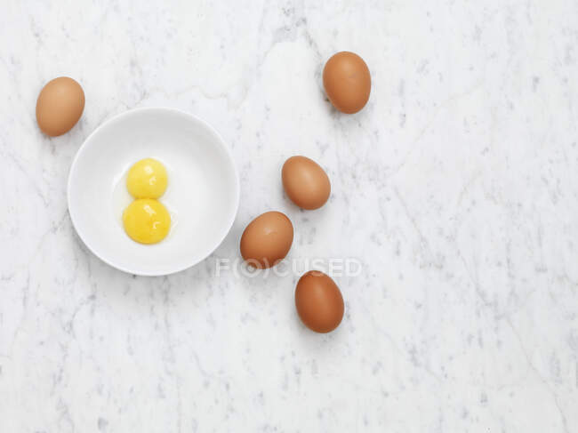 Eier auf Marmoroberfläche und Eigelb in weißer Keramikschale — Stockfoto