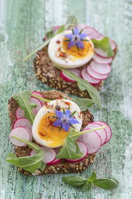 Кусочки хлеба с редиской, вареные половинки яиц и буражные цветы — стоковое фото