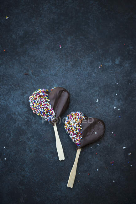 Heart-shaped vegan biscuits on sticks covered with dark chocolate and sprinkles — Stock Photo