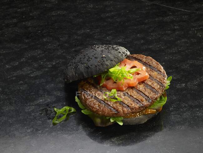 Close-up shot of delicious grilled hamburger on a black bread roll — Stock Photo