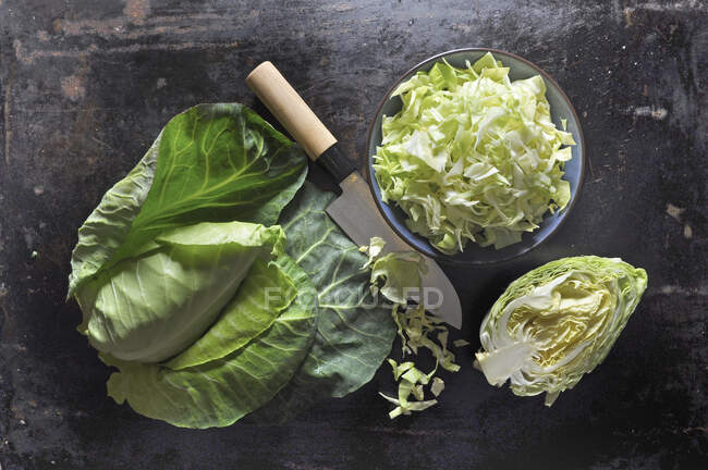 Pointed cabbage, whole, halved and sliced, in a ceramic bowl with a knife on a black baking tray — Stock Photo