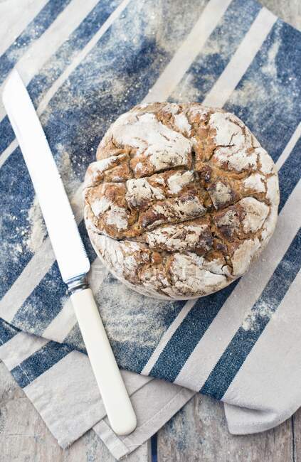 A loaf of homemade sourdough bread on a cloth next to a bag of flour and a knife — Stock Photo