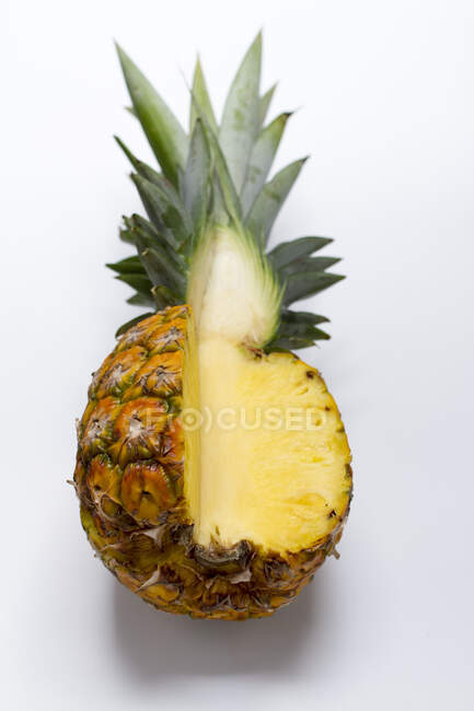 Eine Ananas auf einer weißen Oberfläche, wobei ein Viertel abgeschnitten wird — Stockfoto