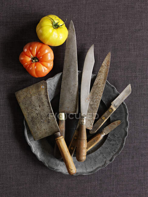 Различные винтажные ножи на оловянной тарелке и помидоры на столе — стоковое фото