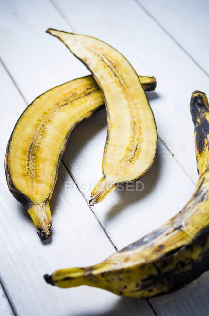 Plátano cortado por la mitad y entero sobre un fondo de madera blanco - foto de stock