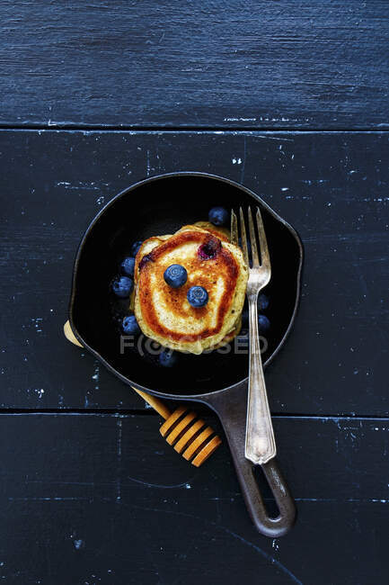 Top view of blueberries homemade pancakes with honey and fresh berries for breakfast in vintage cast iron pan over rustic wooden background — Stock Photo