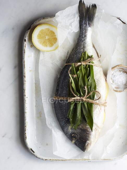 Une brème de mer entière avec de l'ail sauvage sur du papier cuisson — Photo de stock