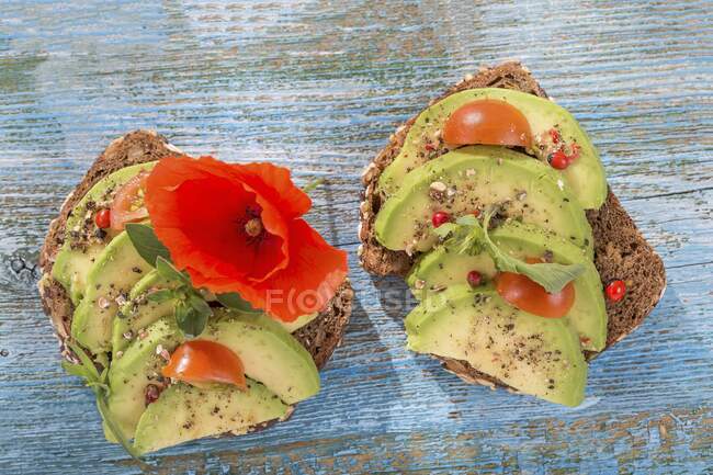 Wholegrain bread topped with avocado slices, tomato and a poppy — Stock Photo