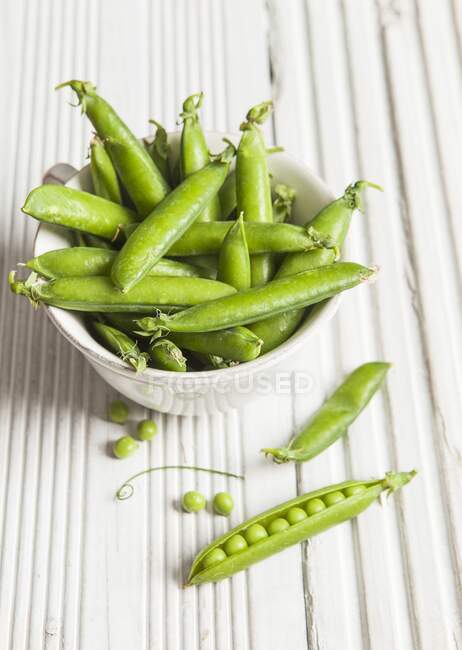 A white bowl full of fresh peas in their pods — Stock Photo