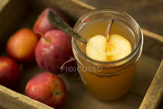 Glass of cider with half of apple and whole apples in wooden crate — Stock Photo