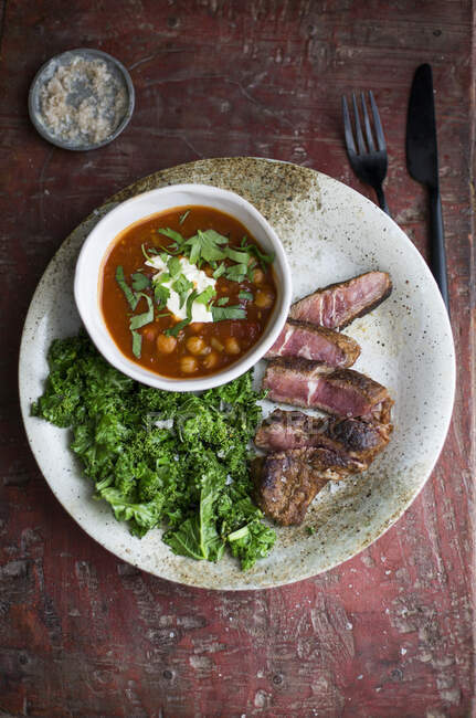 Sliced steak with chickpeas in sauce and kale — Stock Photo