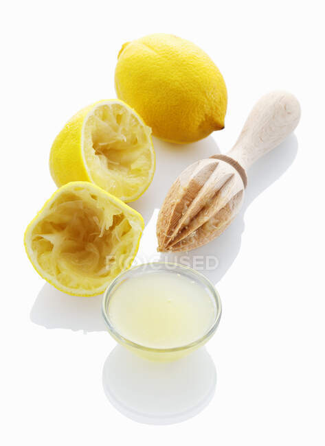 Lemon juice, wooden juicer with juiced and whole lemons — Stock Photo