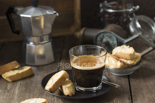 Espresso em um copo e cantuccini com uma cafeteira fogão-top no fundo — Fotografia de Stock