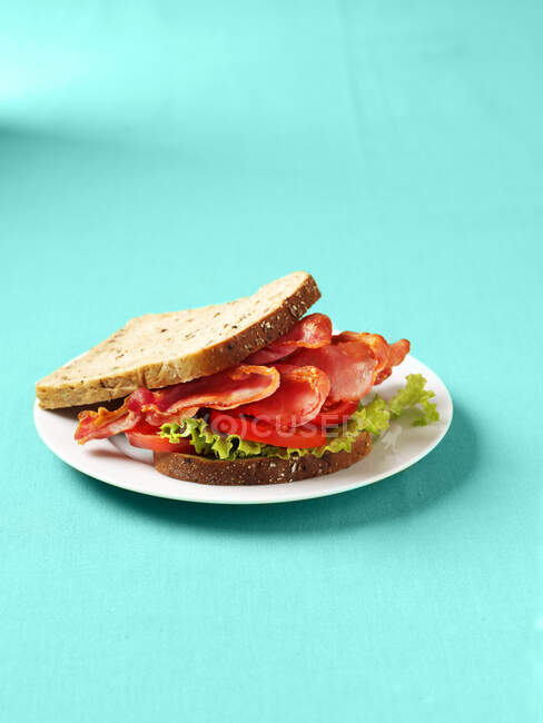 Specksalat und Tomatensandwich auf Teller auf blauem Hintergrund — Stockfoto
