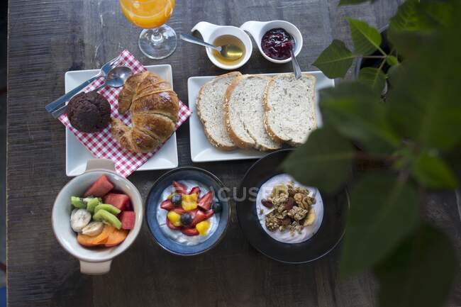 Un desayuno con ensalada de frutas, yogur y muesli, un cruasán, pan blanco y mermelada - foto de stock