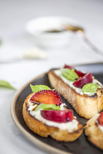 Crostini with plums and basil leaves on plate — Stock Photo