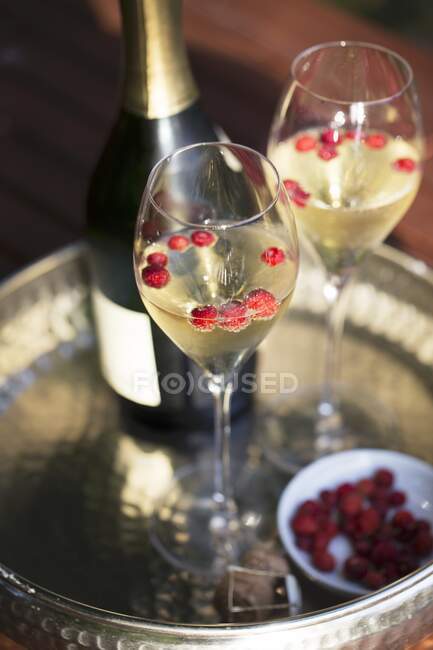 Bottle and two glasses of champagne with wild strawberries on silver tray — Stock Photo
