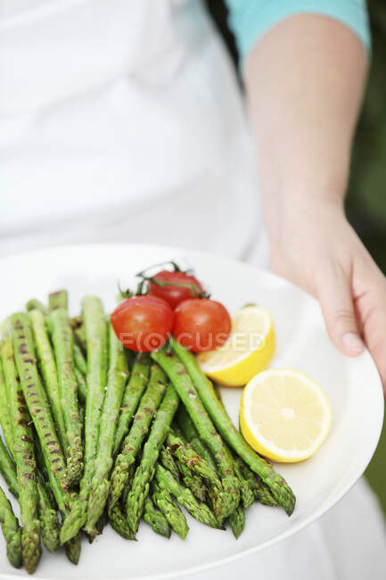 A woman holding a plate of grilled green asparagus — Stock Photo