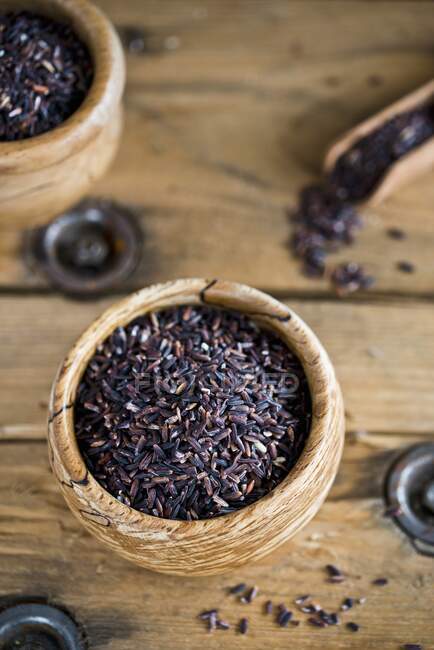 Black rice in wooden bowls with scoop on rustic wooden surface — Stock Photo