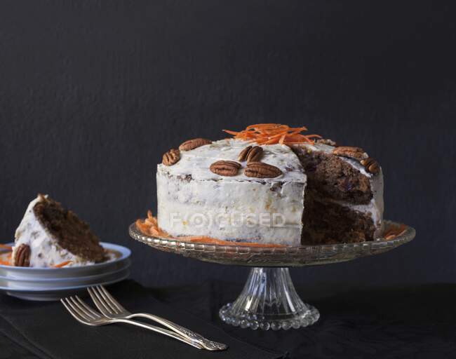 Carrot cake with pecan nuts and a piece missing on a cake stand — Stock Photo